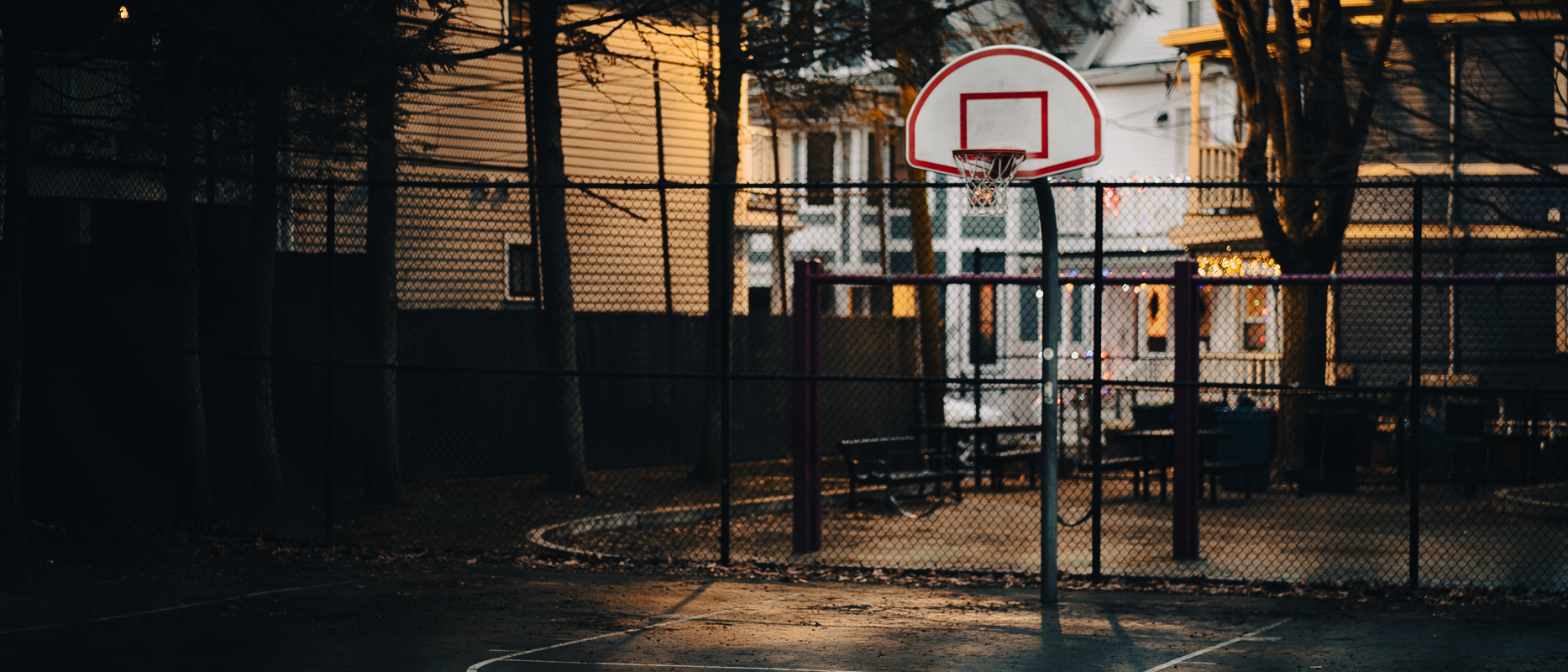 A very dramatic, cinematic photo of a basketball court in front of some houses